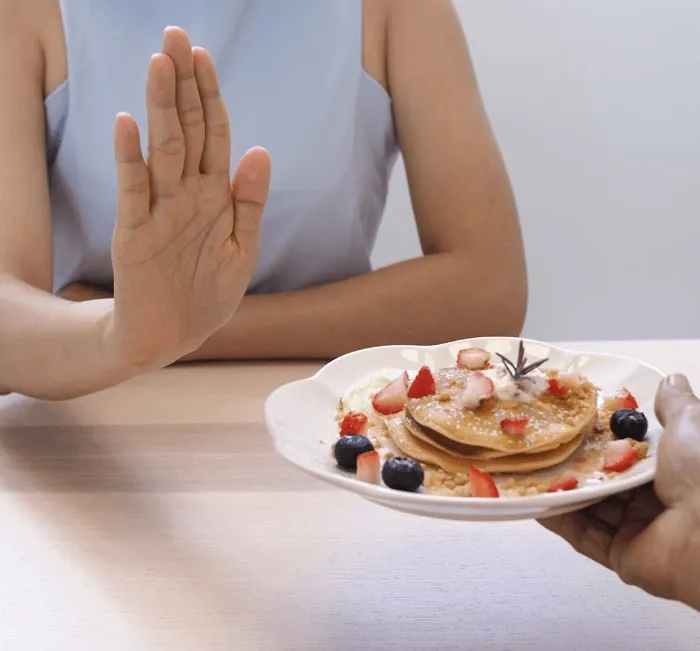 Woman holding up her hand to refuse a plate of pancakes