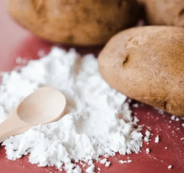 Potatoes beside a pile of white potato starch and a wooden spoon