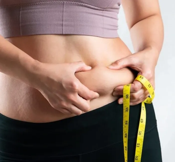 Person pinching the skin at the waist beside a yellow tape measure
